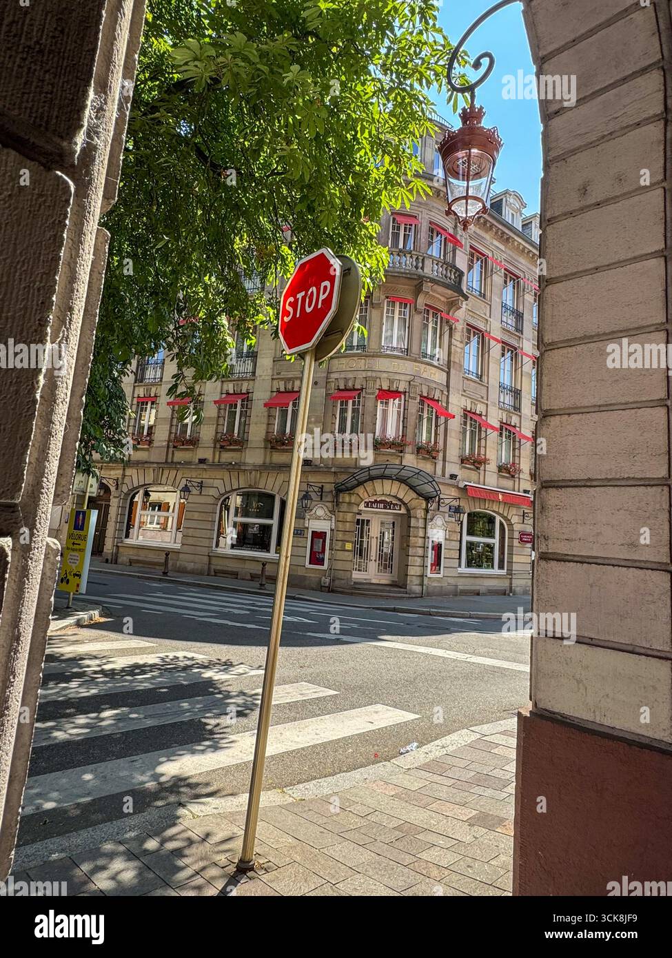 Rue française avec panneau d'arrêt rouge, bâtiment classique en pierre, auvents rouges, balcons en fer forgé et piétons au passage à zèbre. - Image de stock capturée avec un smartphone