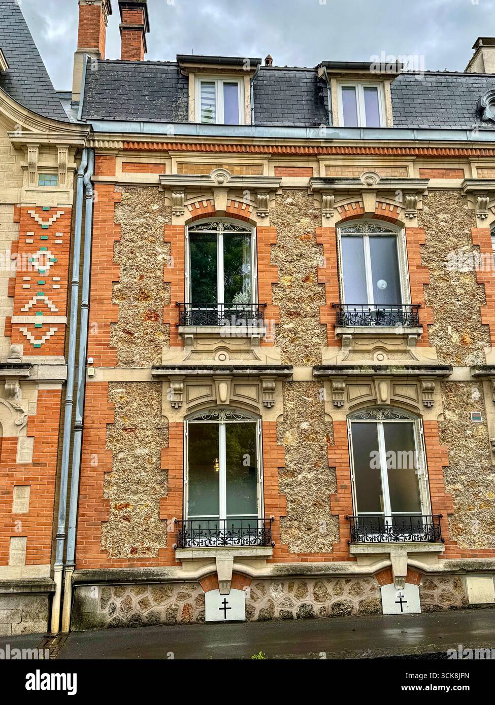 Gros plan sur les fenêtres ornées d'un bâtiment européen historique avec fronts en pierre sculptée, balcons en fer forgé et maçonnerie en briques rouges détaillée - Image de stock capturée avec un smartphone