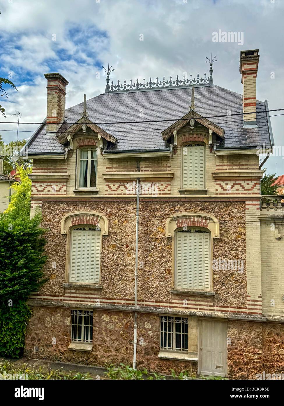 charmante française historique avec façade en pierre et briques, toit en ardoise, cheminées et volets traditionnels entourés de verdure - Image de stock capturée avec un smartphone