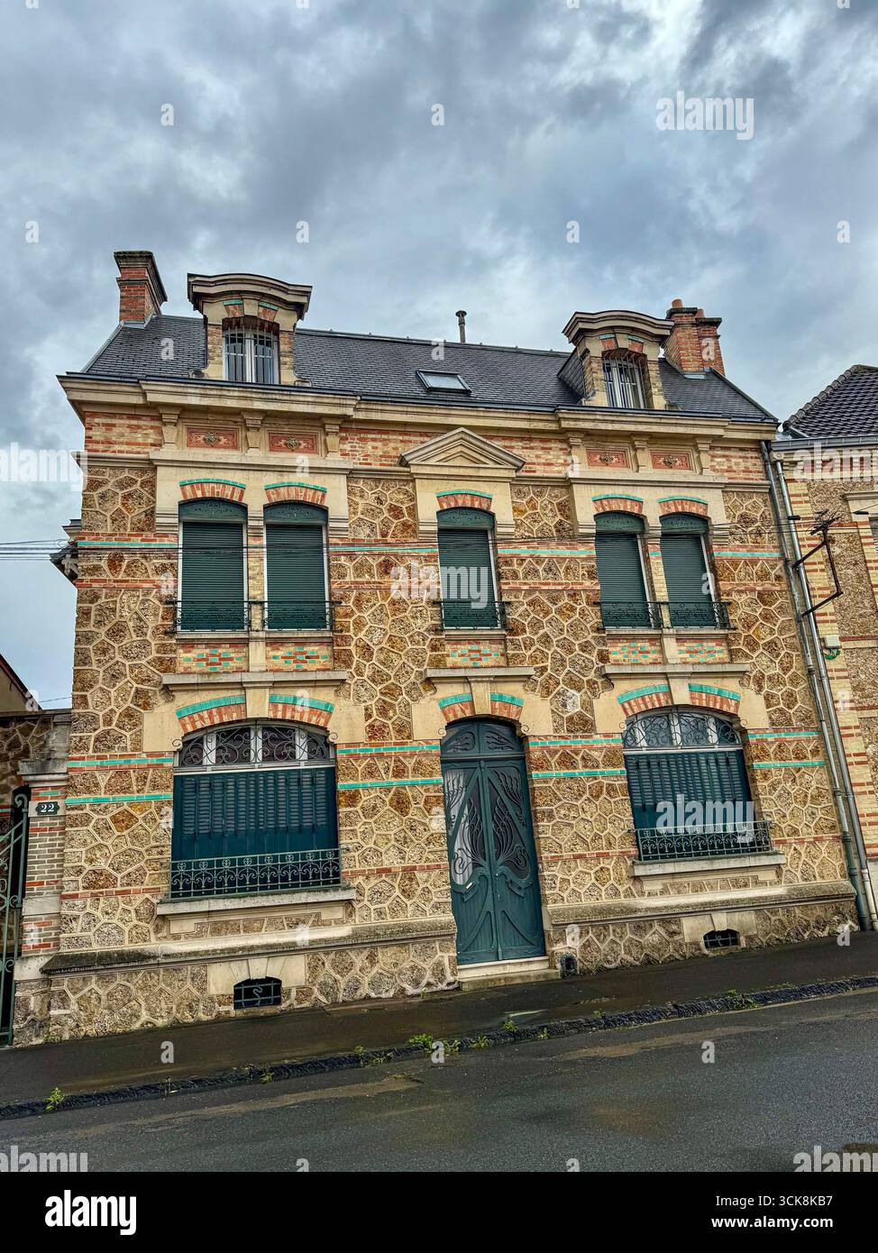 Maison française historique avec façade en pierre et brique, volets verts, toit en ardoise et atmosphère de rue pluvieuse - Image de stock capturée avec un smartphone