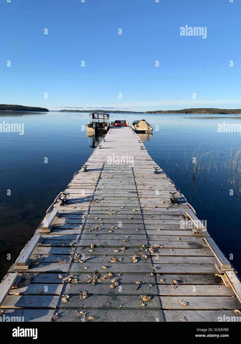 ''quai en bois avec des bateaux sur un lac calme du nord sous un ciel bleu clair, tranquille matin d'automne au Canada.'' - Image de stock capturée avec un smartphone