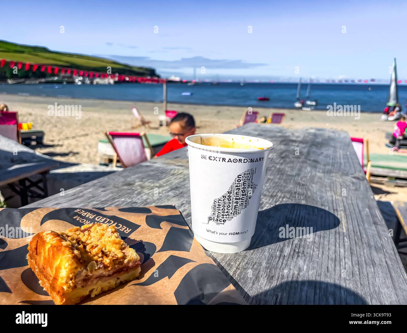 Port Erin, île de Man 08,05,2023 tasse blanche avec les mots 'Blackboard Man' sur elle est assis sur une table en bois à côté d'un morceau de gâteau. La scène est activée Banque D'Images