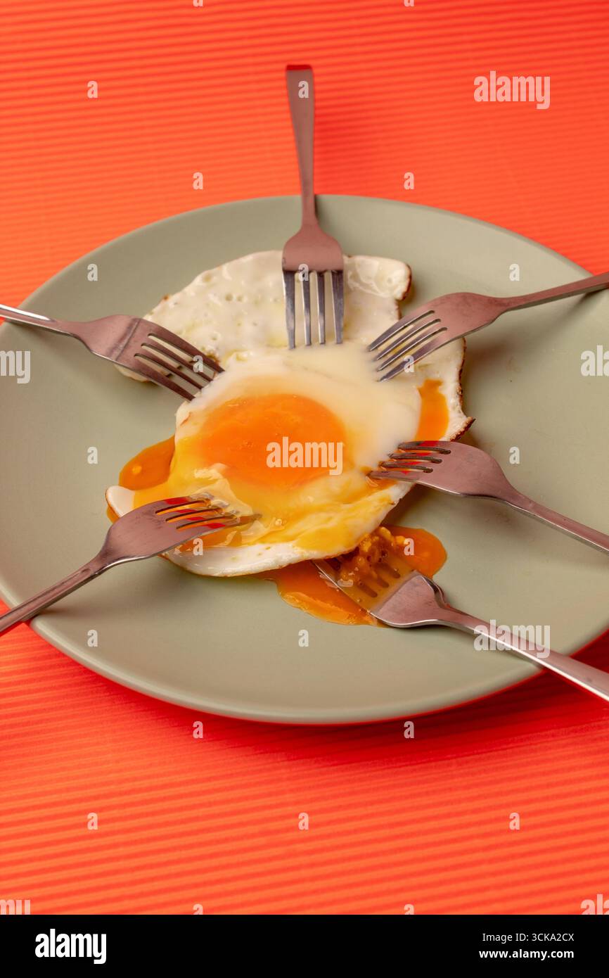 Oeuf frit avec des fourchettes sur une assiette vert pastel avec un fond orange. Pose à plat Banque D'Images