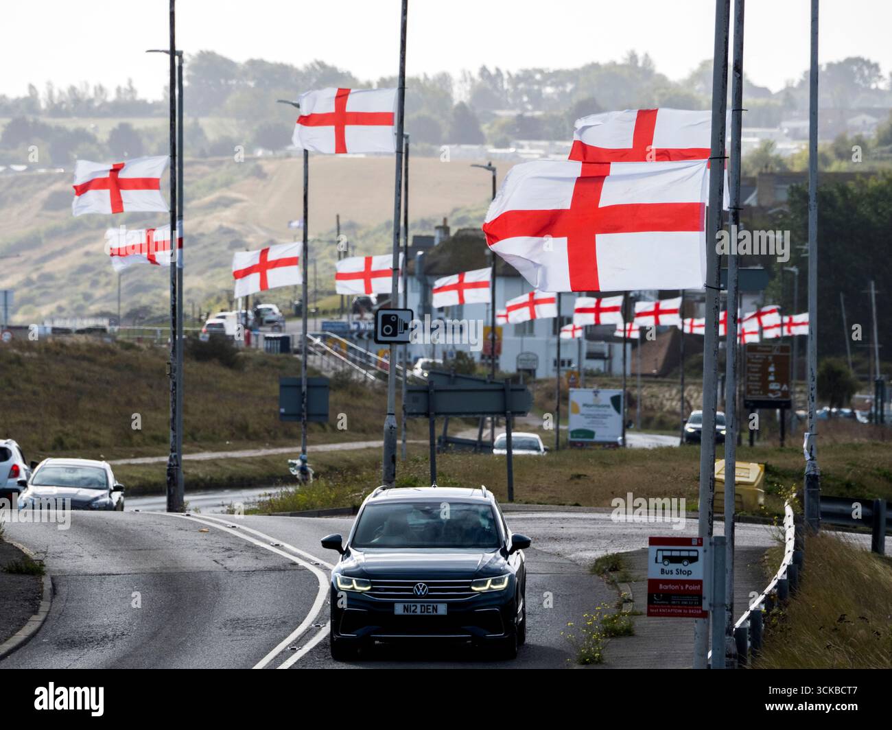 Sheerness, Kent, Royaume-Uni. 11 septembre 2025. Une ligne de drapeaux de St George Cross flottent contre-éclairés par le soleil du matin le long de la route côtière à Sheerness, Kent. L'opération de campagne en ligne Raise the Colours a contribué à augmenter les ventes de drapeaux d'environ 20 pour cent. Crédit : James Bell/Alamy Live News Banque D'Images