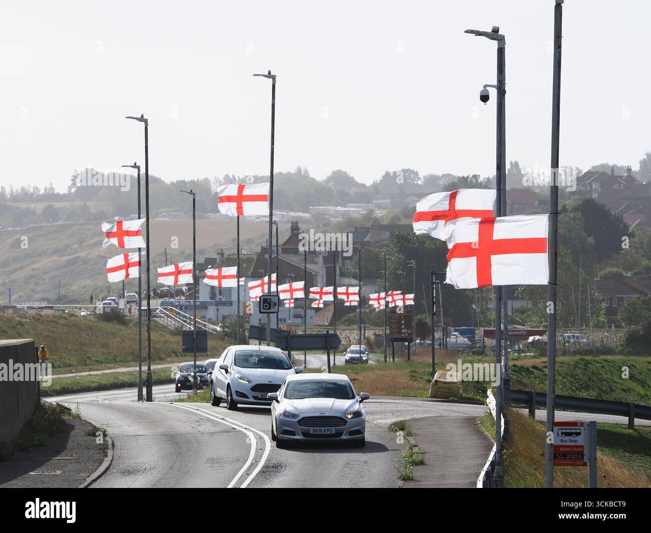 Sheerness, Kent, Royaume-Uni. 11 septembre 2025. Une ligne de drapeaux de St George Cross flottent contre-éclairés par le soleil du matin le long de la route côtière à Sheerness, Kent. L'opération de campagne en ligne Raise the Colours a contribué à augmenter les ventes de drapeaux d'environ 20 pour cent. Crédit : James Bell/Alamy Live News Banque D'Images