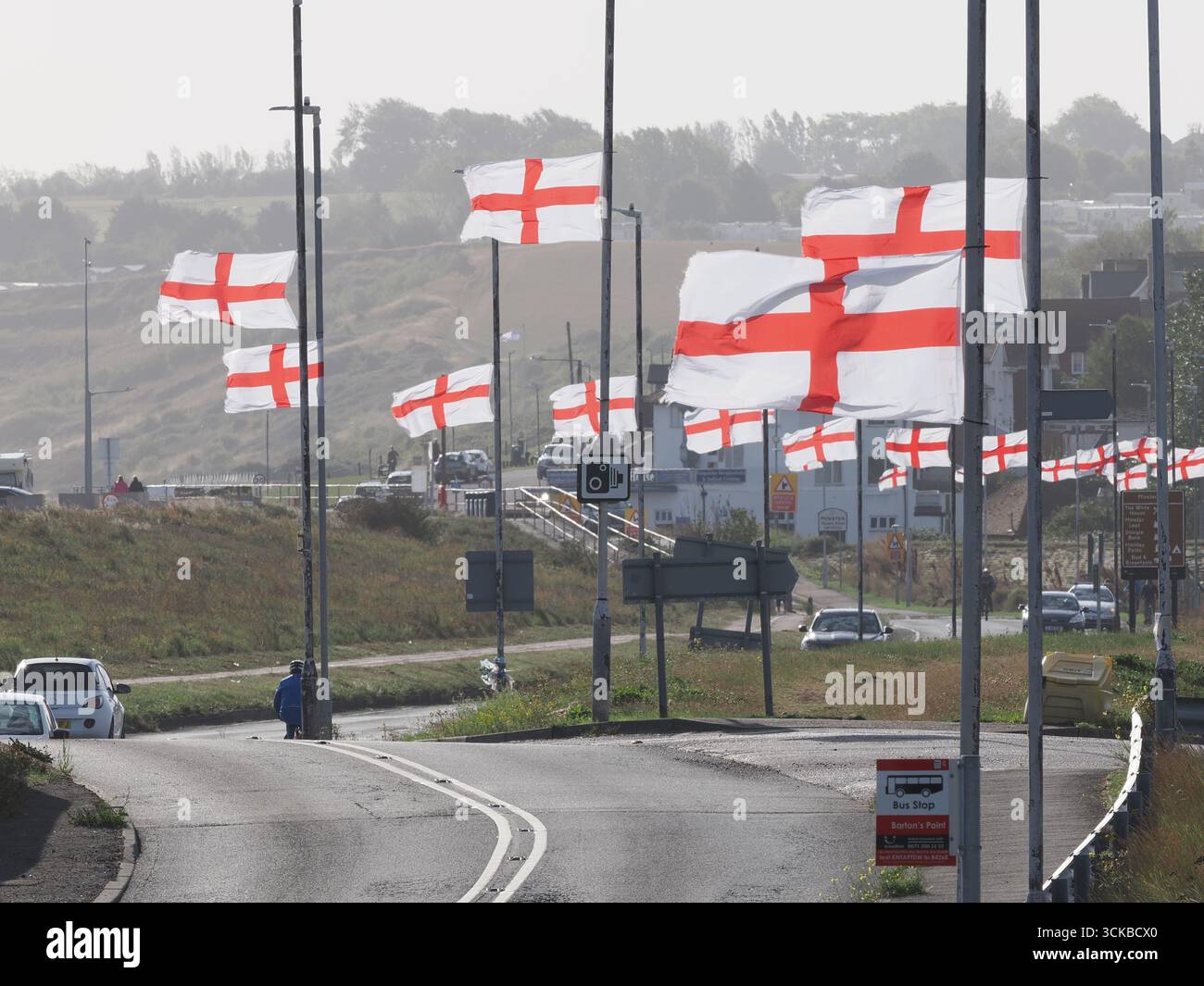 Sheerness, Kent, Royaume-Uni. 11 septembre 2025. Une ligne de drapeaux de St George Cross flottent contre-éclairés par le soleil du matin le long de la route côtière à Sheerness, Kent. L'opération de campagne en ligne Raise the Colours a contribué à augmenter les ventes de drapeaux d'environ 20 pour cent. Crédit : James Bell/Alamy Live News Banque D'Images