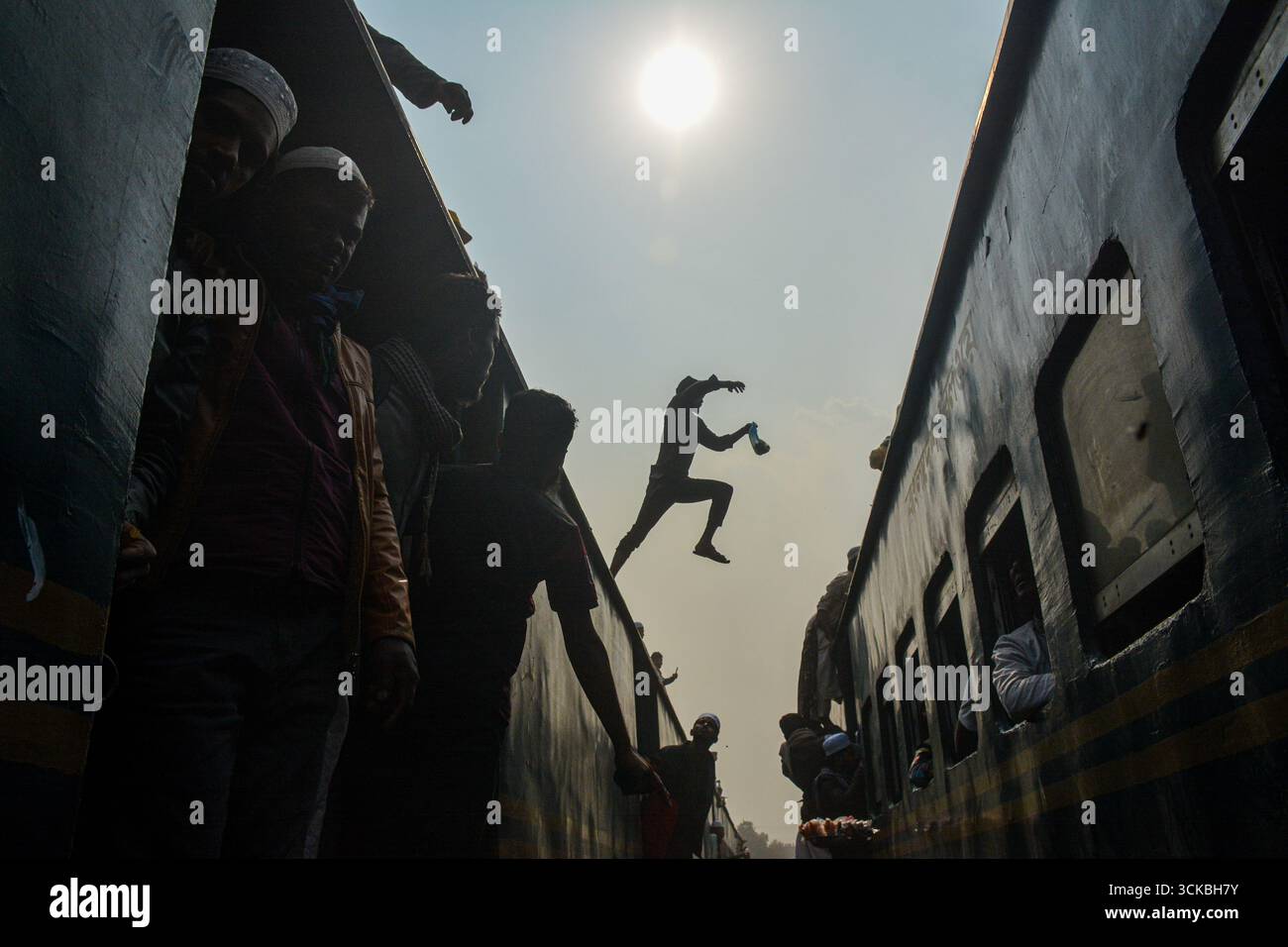 Dhaka, Bangladesh - 15 janvier 2023 : vue d'un saut audacieux entre des trains bondés sous le soleil brumeux, des silhouettes contrastant avec le ciel lumineux, un moment de transit précaire capturé à Dhaka. Banque D'Images