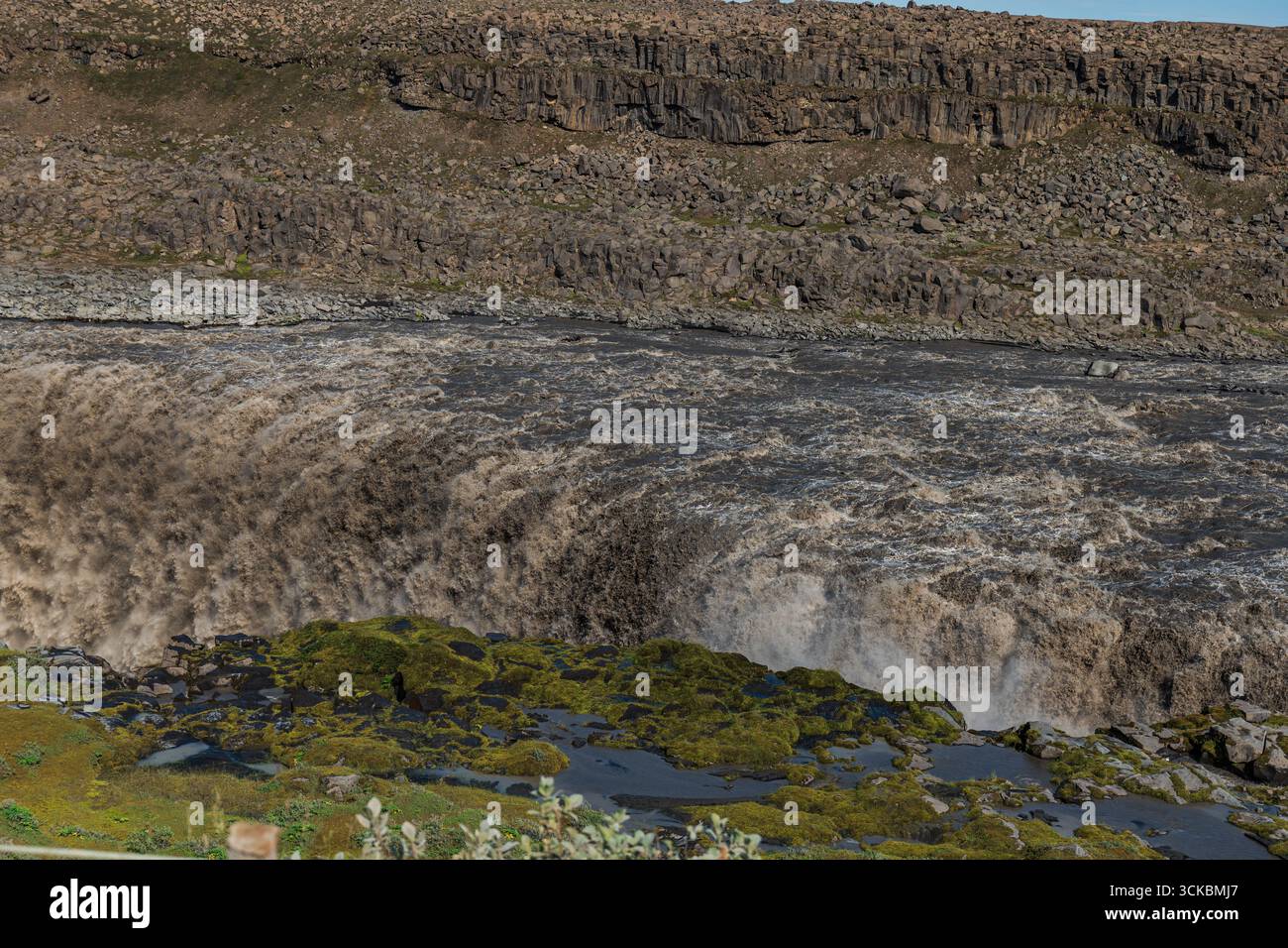 Les cascades de Dettifoss avec une immense eau boueuse sur des falaises accidentées, entourées de terrains rocheux, de mousse verte et de formations de basalte. Banque D'Images