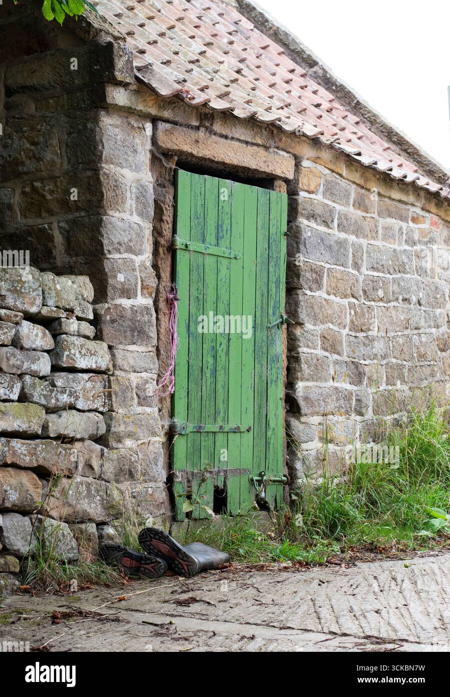 Un bâtiment rustique en pierre avec une porte peinte en vert vieilli et des bottes wellington posées sur le sol. Banque D'Images