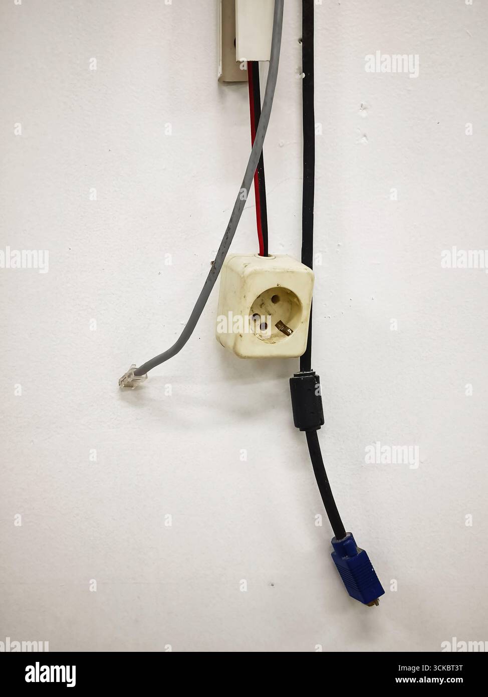 Une vieille prise murale électrique avec des câbles téléphoniques et VGA suspendus lâchement autour. Banque D'Images
