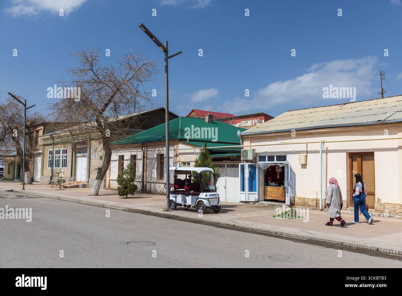 Boukhara, Ouzbékistan - 27 mars 2024 : les gens marchent dans la rue dans la vieille ville de Boukhara par une journée ensoleillée. Vieilles petites maisons résidentielles et magasins locaux se tiennent Banque D'Images