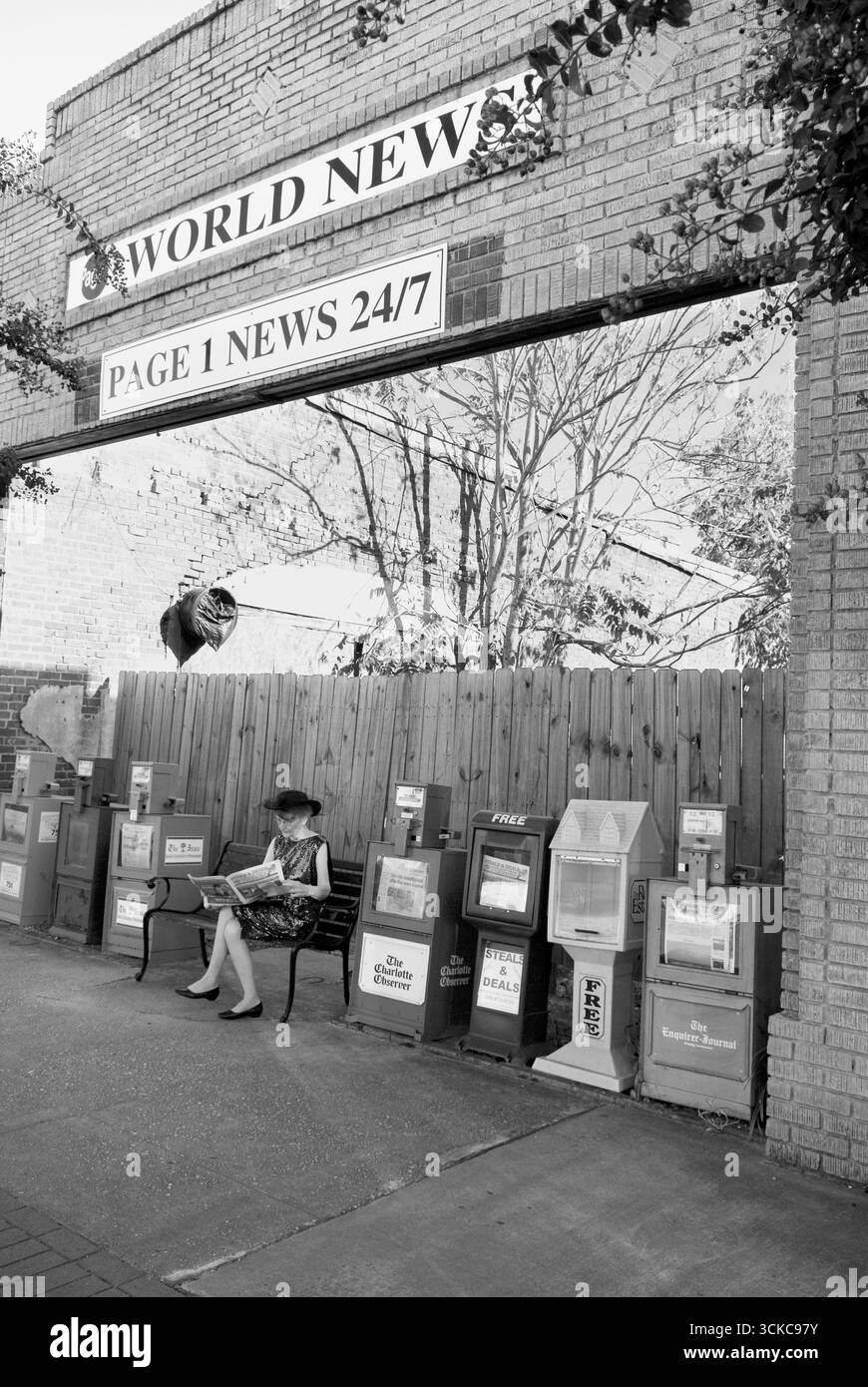 Femme caucasienne assise seule sur le banc dans un kiosque à journaux de petite ville lisant un journal à Pageland, Caroline du Sud, États-Unis. Banque D'Images