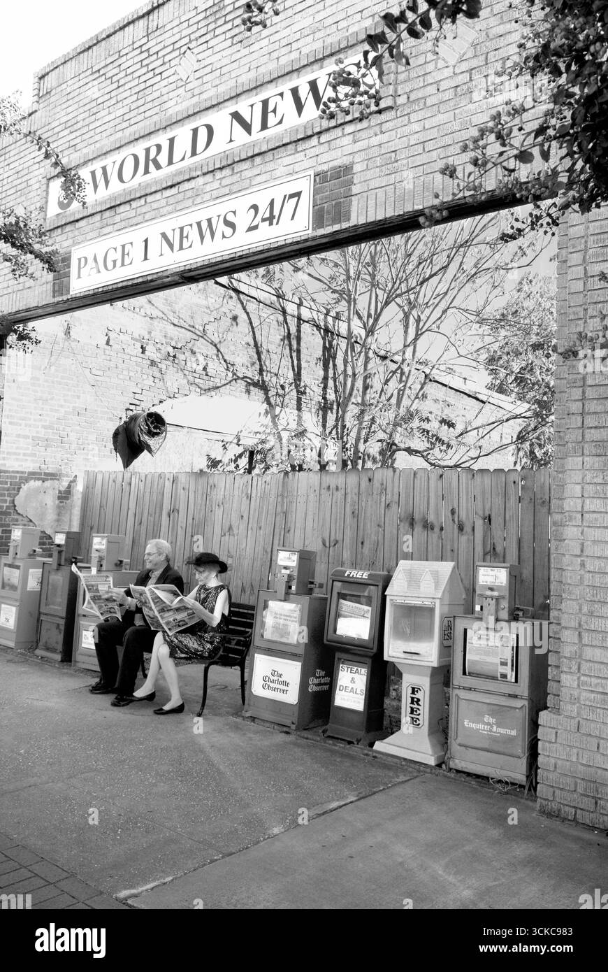Couple caucasien assis sur un banc dans un kiosque à journaux d'une petite ville lisant des journaux à Pageland, Caroline du Sud, États-Unis. Banque D'Images