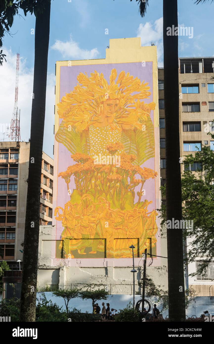 Grande murale de jeune femme avec des fleurs et des gens dansants peints dans des couleurs jaunes et vertes douces. Cali, Valle del Cauca Department,, Colombie Banque D'Images