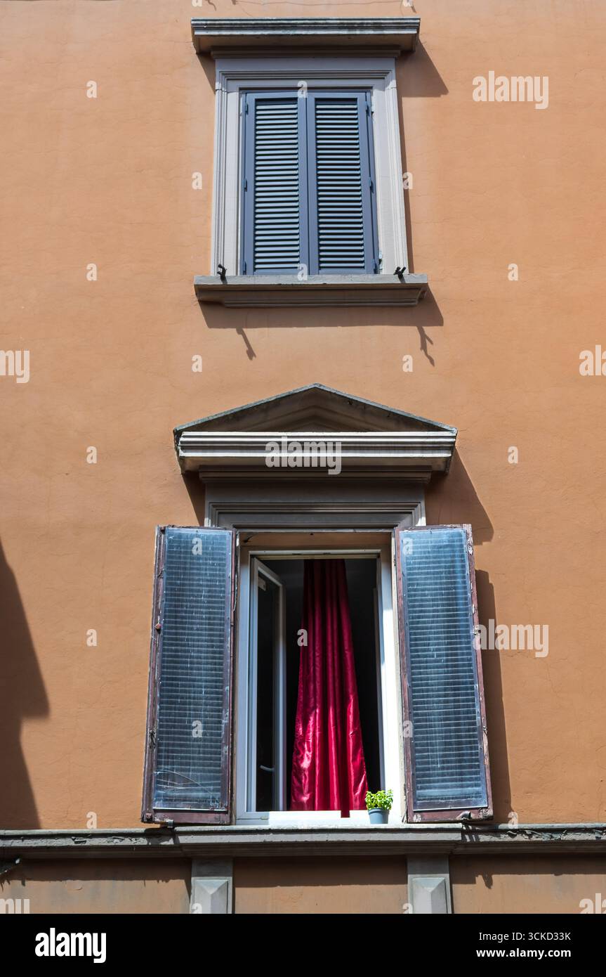 mur orange avec volets bleus et rideaux rouges avec deux fenêtres et une plante Banque D'Images