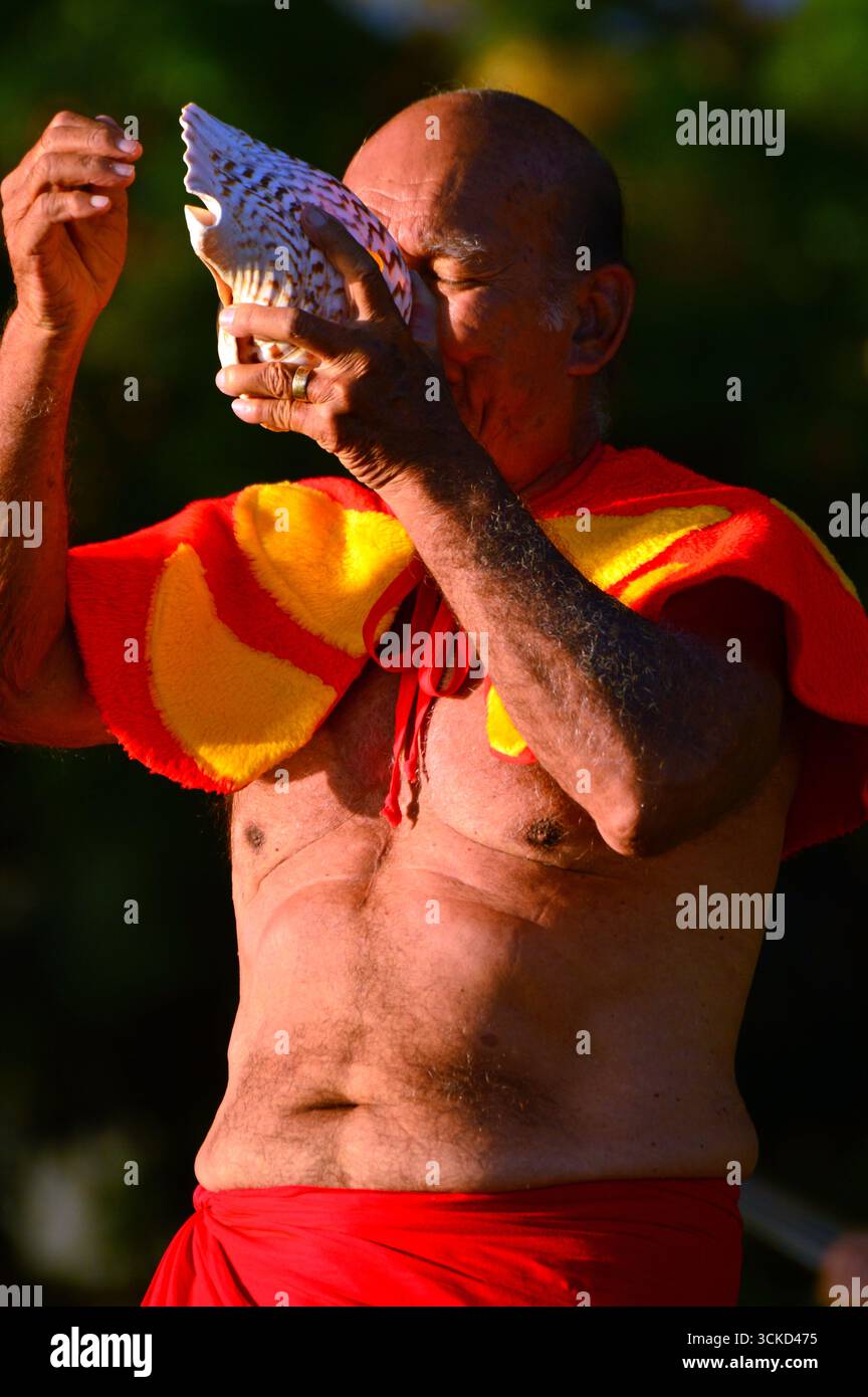 Un homme aîné signale le début des festivités en soufflant dans une coquille de conque sur Waikiki Beach Hawaii Banque D'Images