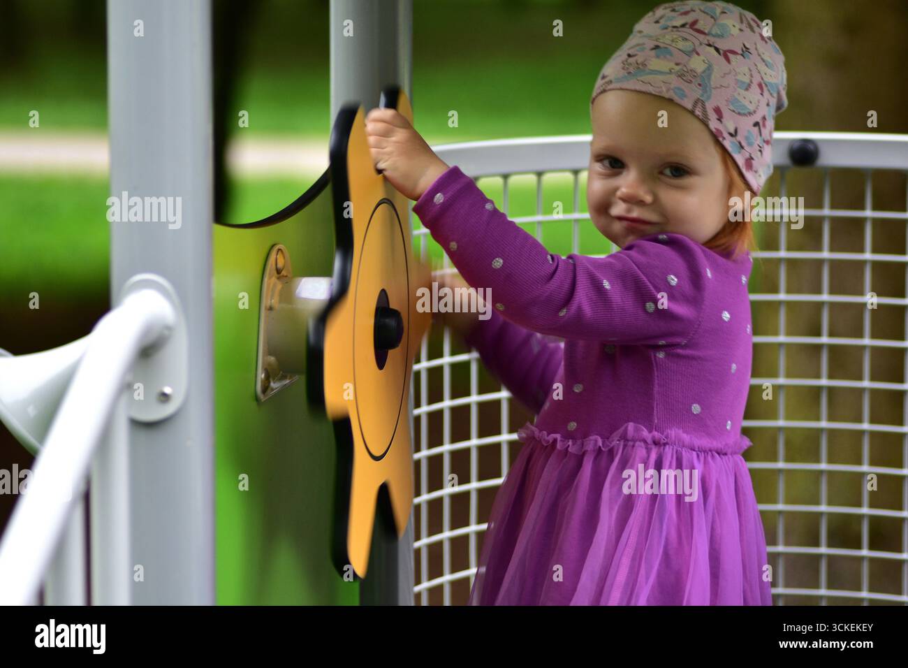 Mignon jeune fille en robe violette souriant et jouant avec le jouet jaune volant à l'aire de jeux. Enfant profitant du plaisir et de l'imagination en plein air pendant Banque D'Images