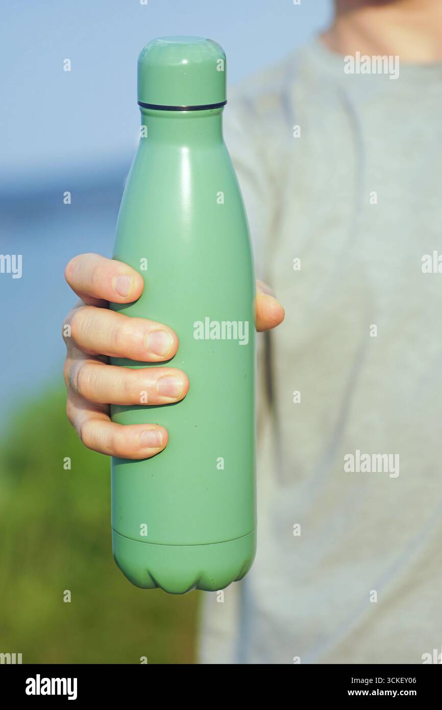 Man propose une bouteille en métal réutilisable. La personne remet les thermos. Engagement individuel en matière d’action climatique, responsabilité écologique et impact écologique positif Banque D'Images