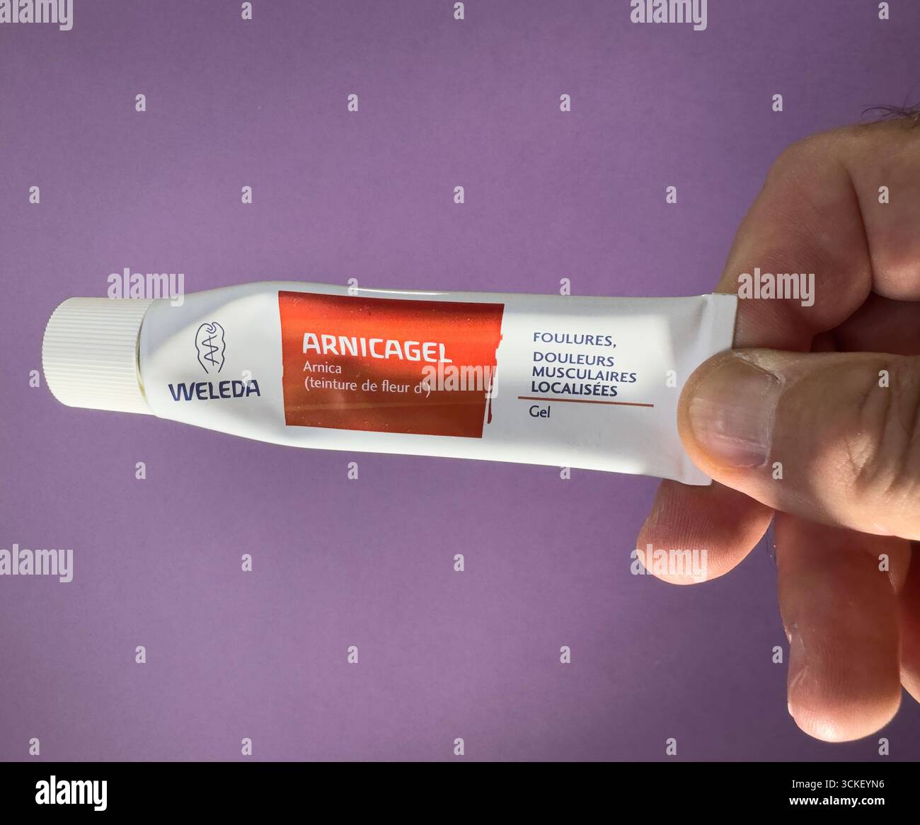 Paris, France - Sep 2, 2025 : main tenant le tube Weleda Arnicagel pour le soulagement de la douleur musculaire sur fond violet avec l'accent sur le produit Banque D'Images