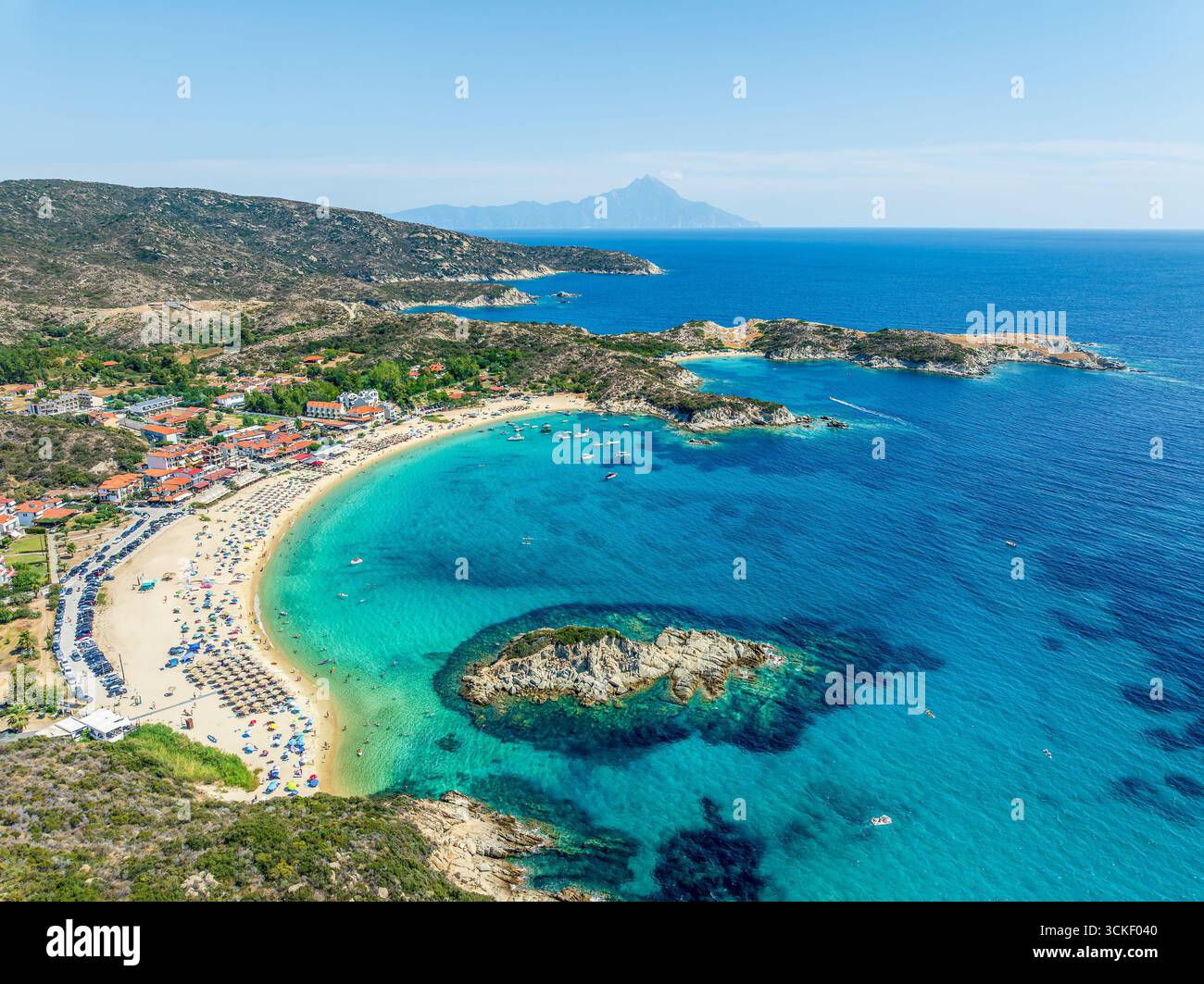 Vue aérienne de la plage de Kalamitsi à Sithonia, Grèce, avec des eaux turquoises, sable doré, parasols, un village balnéaire, et le mont Athos dans le bac Banque D'Images