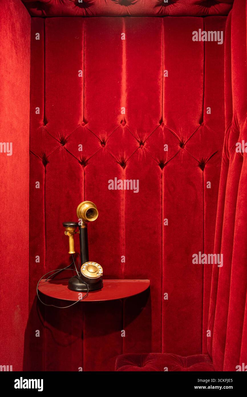 Des murs en velours rouge moelleux encadrent un téléphone en forme de chandelier doré dans cette cabine d'inspiration vintage, idéale pour les thèmes éditoriaux, cinématographiques ou historiques Banque D'Images