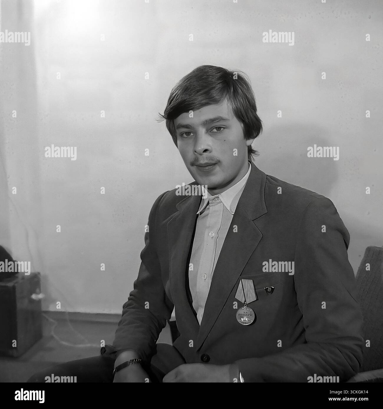 Portrait d'un membre du Komsomol, un étudiant diplômé ou supérieur de l'école n° 12 de Sloviansk, pris à la fin des années 1970, qui porte fièrement un badge GTO ('prêt pour le travail et la défense') sur sa poitrine. Sa coupe de cheveux à la mode et son attitude confiante symbolisent la jeunesse soviétique idéale pendant la stagnation de l'ère Brejnev : éduquée, en forme physique et fidèle aux idéaux inculqués par le vaste système éducatif patriotique de l'État. Le programme GTO était un élément clé de cet entraînement prémilitaire Banque D'Images