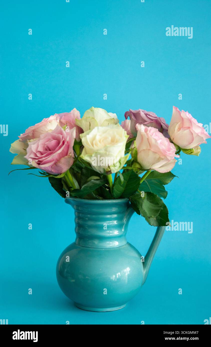 Bouquet de roses roses et blanches dans un vase en céramique bleue sur un fond mural texturé Banque D'Images