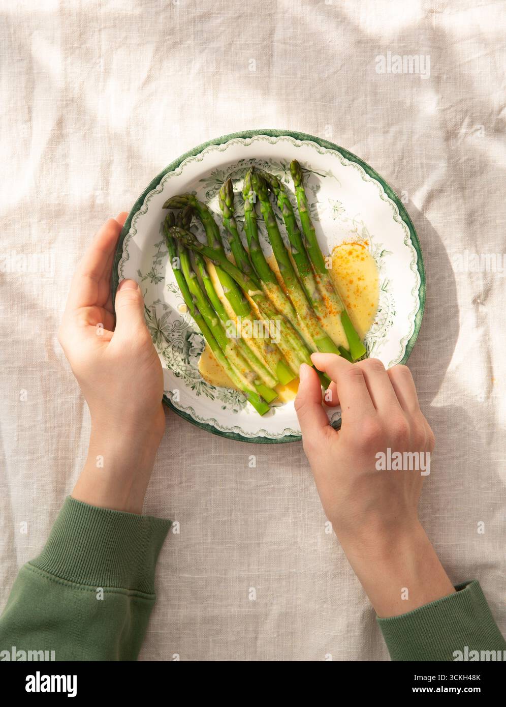 Image à plat d'une paire de mains avec une assiette d'asperges, asperges officinalis et sauce hollandaise Banque D'Images