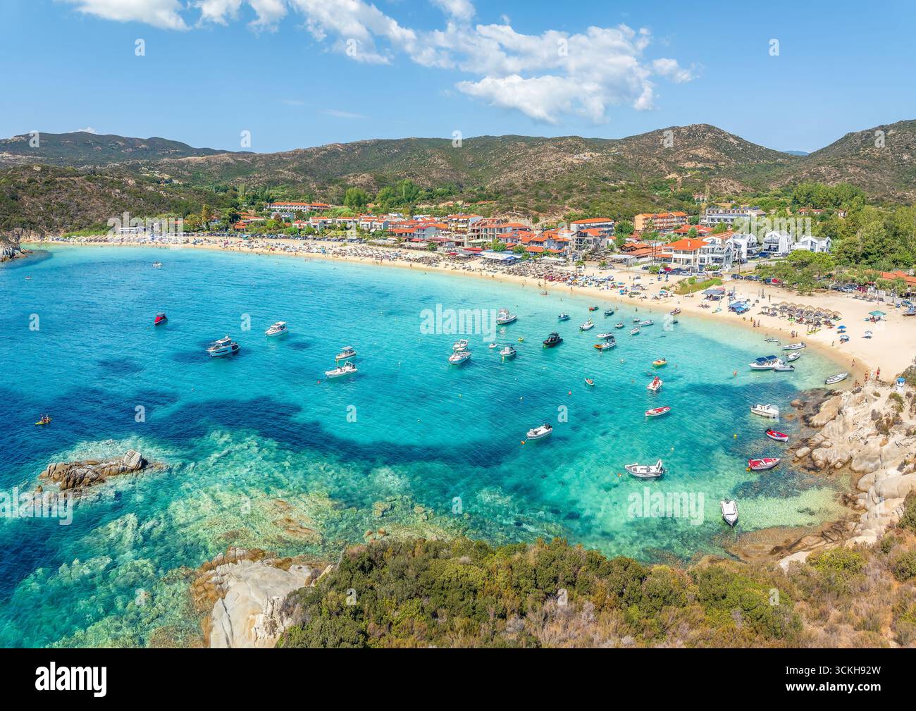 Vue aérienne de la plage de Kalamitsi à Sithonia, Grèce, avec des eaux turquoises, sable doré, parasols, îlots rocheux, et une villa traditionnelle en bord de mer Banque D'Images