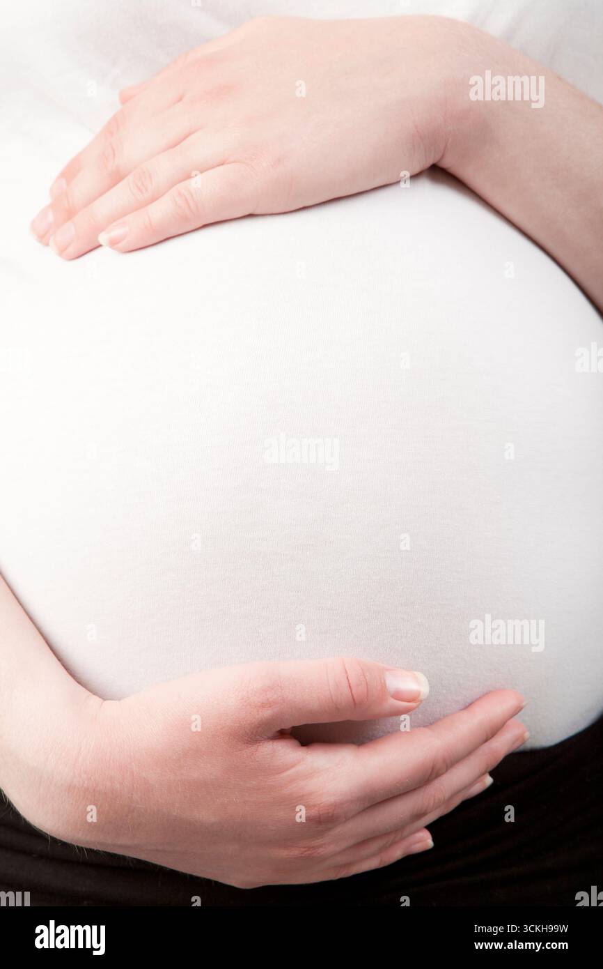 Ventre enceinte tendu tendrement par les mains, symbolisant l'amour maternel, la protection et l'anticipation sereine de la maternité sur fond blanc Banque D'Images