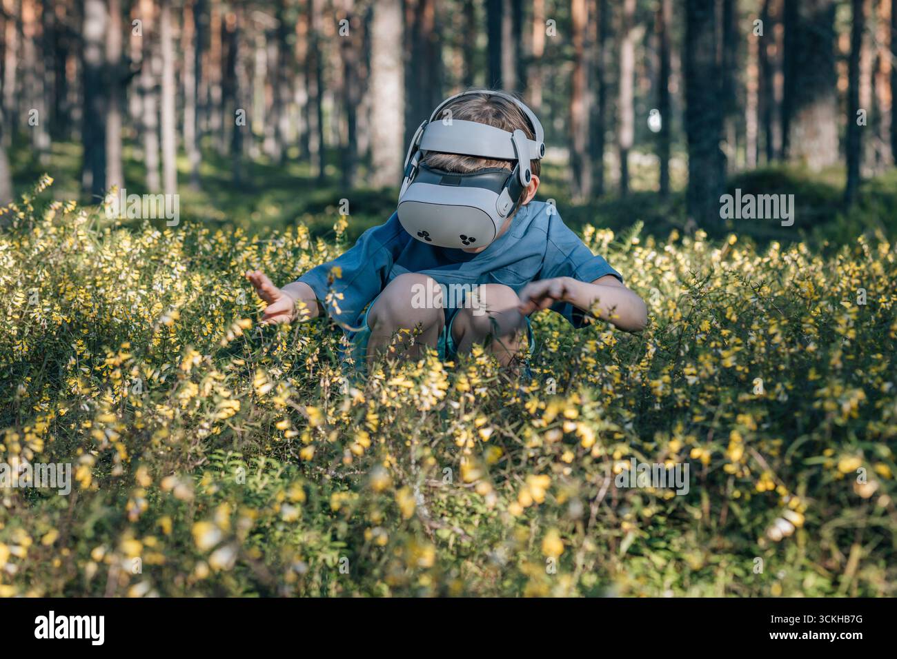 Enfant dans des lunettes virtuelles regarde les fleurs dans la forêt Banque D'Images