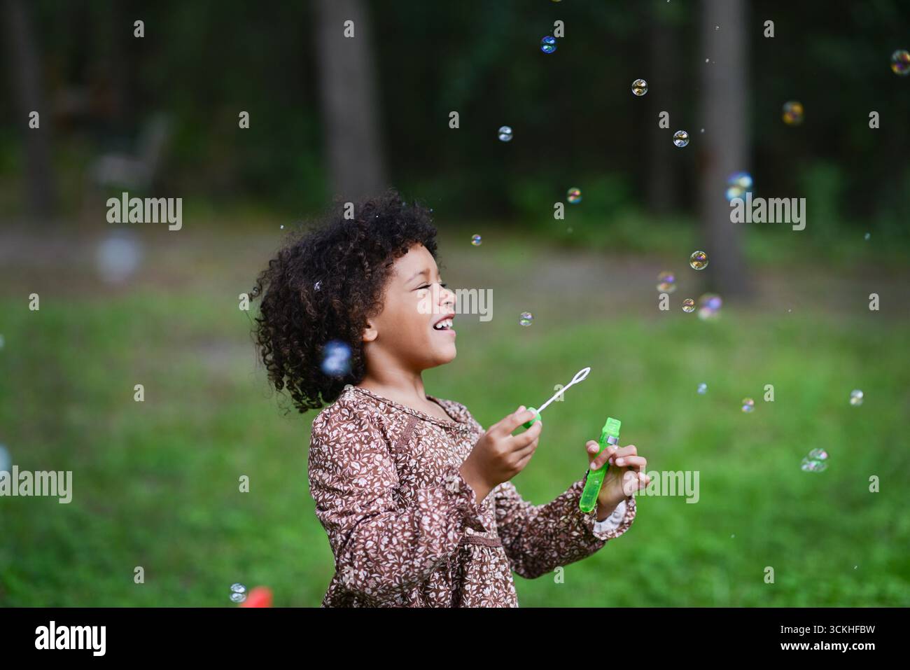 La fille riante souffle des bulles dans l'espace extérieur herbeux. Banque D'Images
