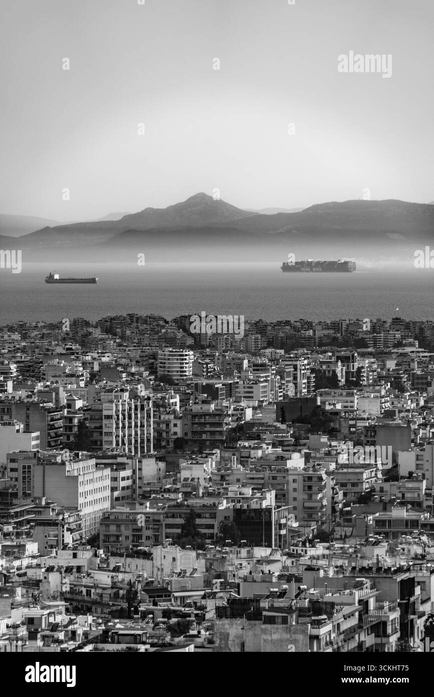 Vue d'Athènes à travers le golfe Saronique avec des cargos et des cargos en mer, des montagnes côtières brumeuses à l'horizon et les toits urbains du c Banque D'Images