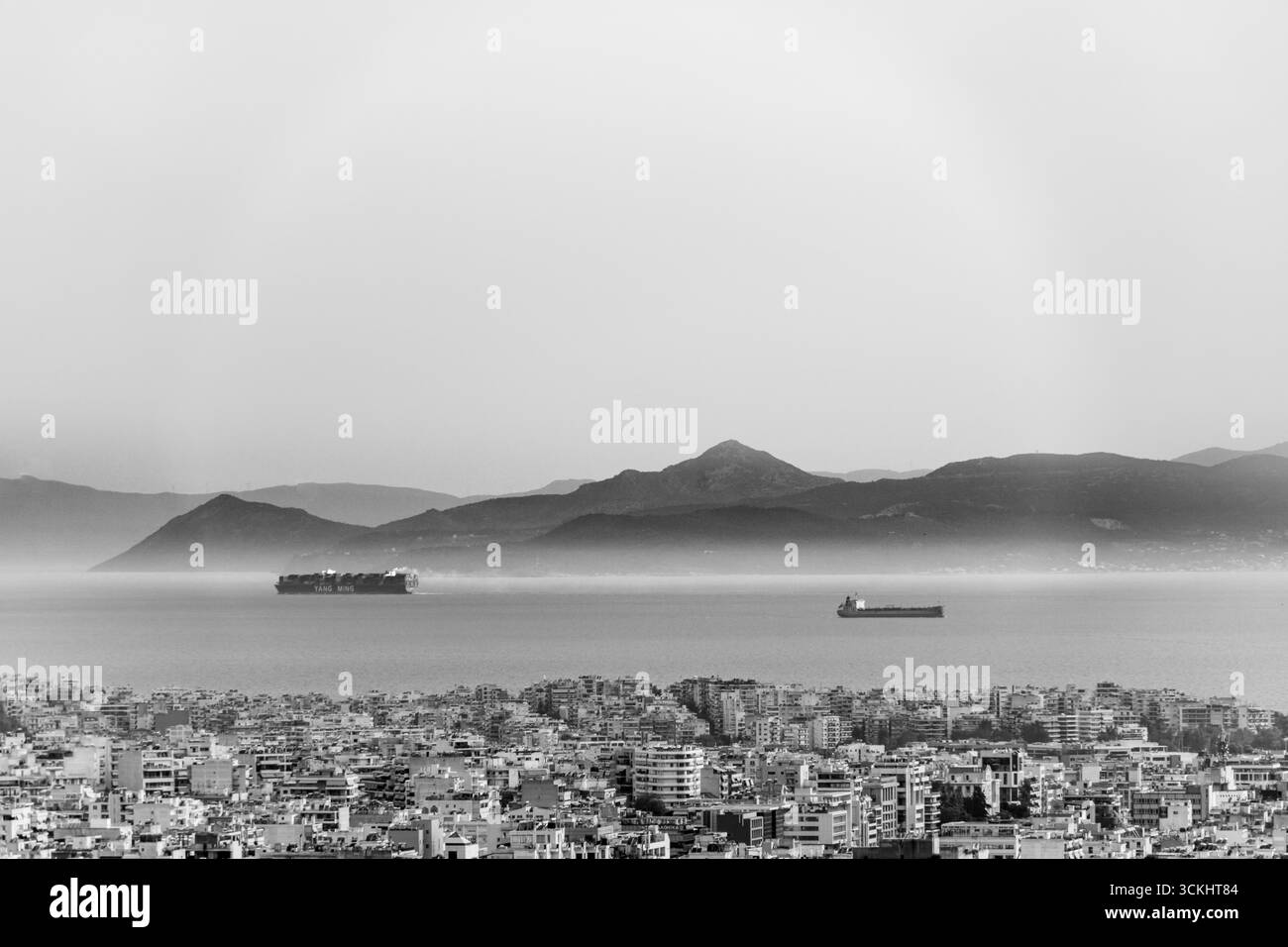 Panorama au large d'Athènes vers le golfe Saronique avec des porte-conteneurs traversant des eaux calmes et des montagnes bleues à l'horizon lointain, la ville construite Banque D'Images