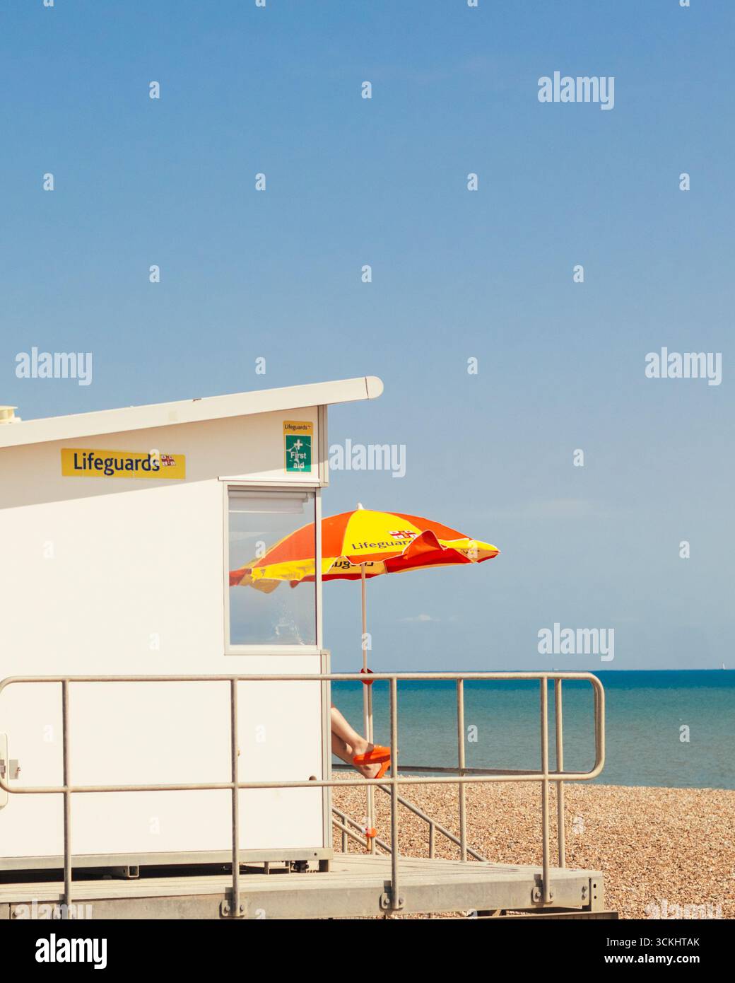 Un sauveteur en service, assis dans la cabane des sauveteurs sur la plage par une journée ensoleillée à Hastings Banque D'Images