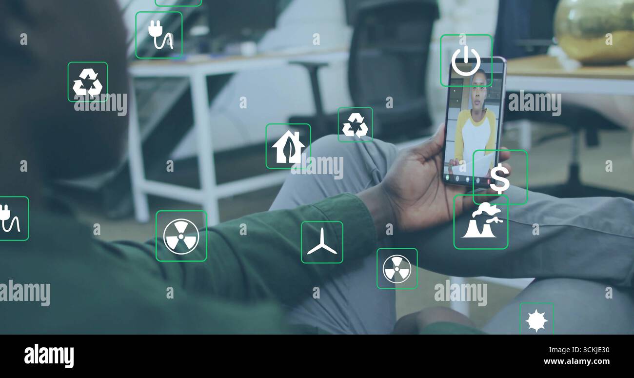 Tenant smartphone homme afro-américain visionnant l'appel virtuel sur le sol du bureau, avec des icônes d'énergie Banque D'Images