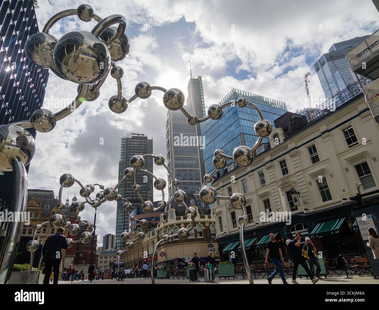 Les piétons passent devant Infinite accumulation de Yayoi Kusama, commandée par la fondation artistique crossrail à l'extérieur du 100 Liverpool Street London UK, avec des gratte-ciel en arrière-plan sur un ciel sombre Banque D'Images