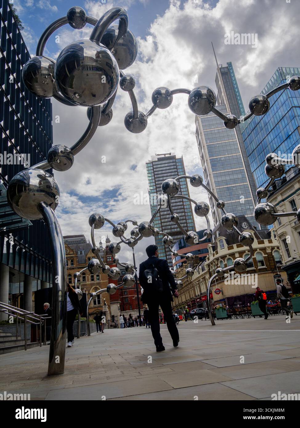 Les piétons passent devant Infinite accumulation de Yayoi Kusama, commandée par la fondation artistique crossrail à l'extérieur du 100 Liverpool Street London UK, avec des gratte-ciel en arrière-plan sur un ciel sombre Banque D'Images