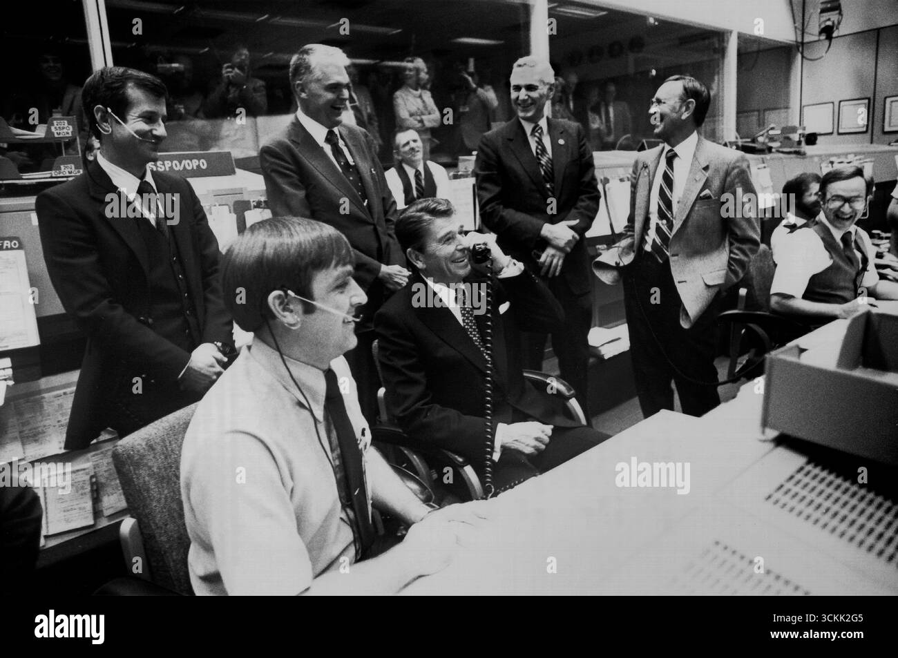 HOUSTON, TEXAS, États-Unis - 13 novembre 1981 - le président américain Ronald Reagan se moque des responsables de la NASA dans Mission Control quand il demande en plaisantant aux membres d'équipage, les astronautes Joe Engle et Richard Truly s'ils pouvaient s'arrêter à Washington en route vers leur site d'atterrissage en Californie afin qu'il puisse venir. L'équipage du STS-2 était dans son avant-dernier jour sur orbite lorsque la conversation a eu lieu. De gauche à droite debout : Terry J. Hart, administrateur adjoint de la NASA Dr Hans Mark, administrateur de la NASA James M. Beggs, directeur de la JSC Dr Christopher C. Kraft Jr. De gauche à droite assis : CAPCOM, astronaute Banque D'Images