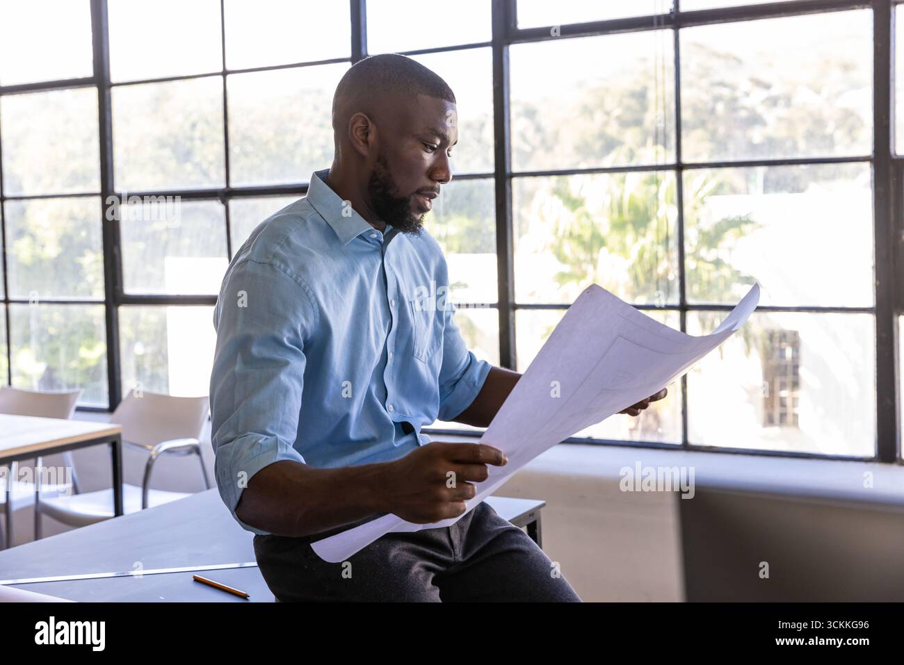 Homme afro-américain examinant les plans architecturaux sur la table à l'intérieur du studio de design Banque D'Images