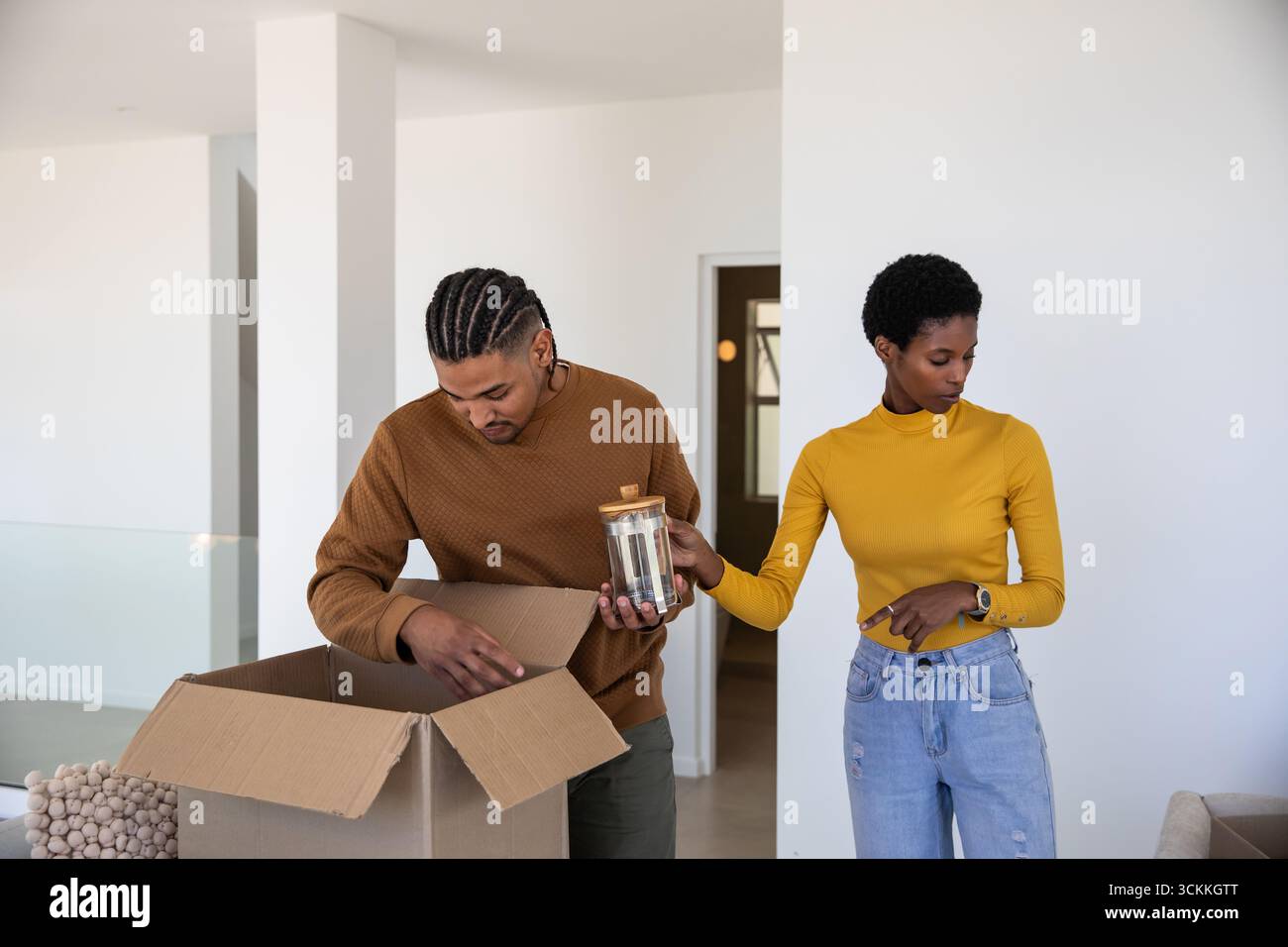 Couple diversifié déballage de la boîte en carton dans le salon moderne avec pot en verre et couvercle en bois Banque D'Images