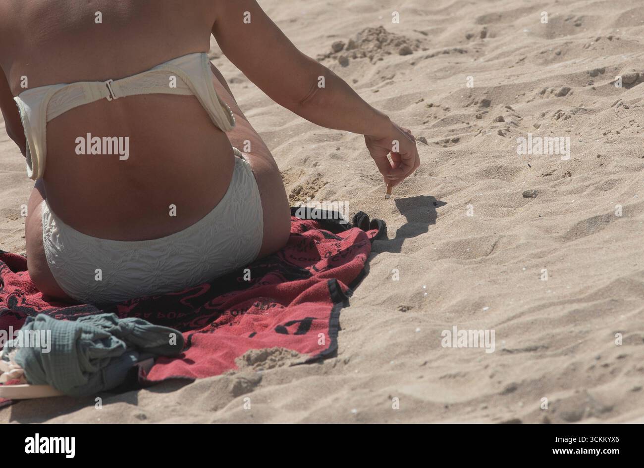 Palma, Espagne. 12 septembre 2025. Une femme jette une cigarette dans le sable sur la plage d'Arenal à Majorque. Un projet de loi visant à étendre les zones sans fumée a été adopté en Espagne cette semaine. Crédit : Clara Margais/dpa/Alamy Live News Banque D'Images