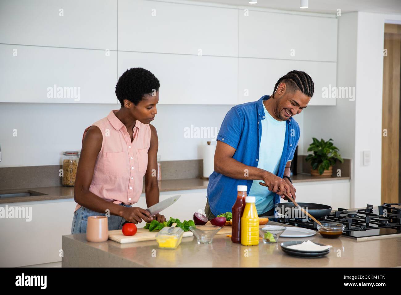 Cuisine de couple diversifiée sur l'îlot de cuisine, hacher la laitue et remuer la sauce dans une poêle Banque D'Images Cuisine de couple diversifiée sur l'îlot de cuisine, hacher la laitue et remuer la sauce dans une poêle Banque D'Images
