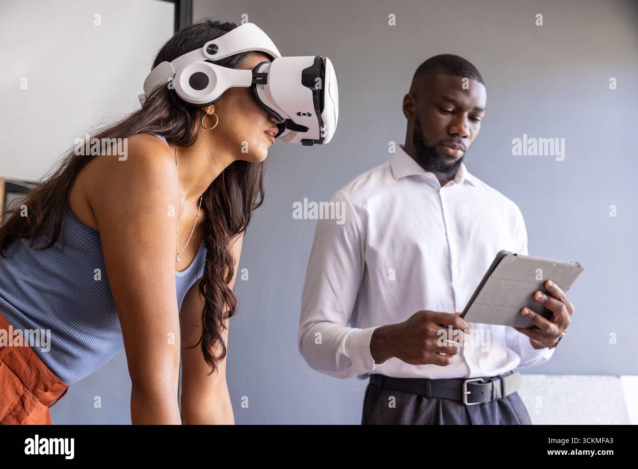 Divers collègues faisant la démonstration d'un casque de réalité virtuelle, dans une salle de réunion avec tablette, tableau blanc Banque D'Images