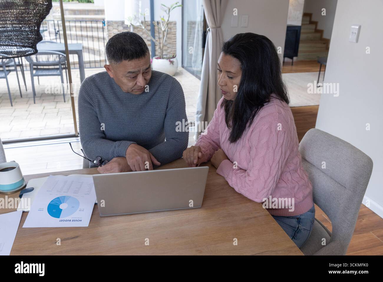 Couple senior examinant les feuilles de budget imprimées, discutant des finances à la table à manger avec ordinateur portable Banque D'Images