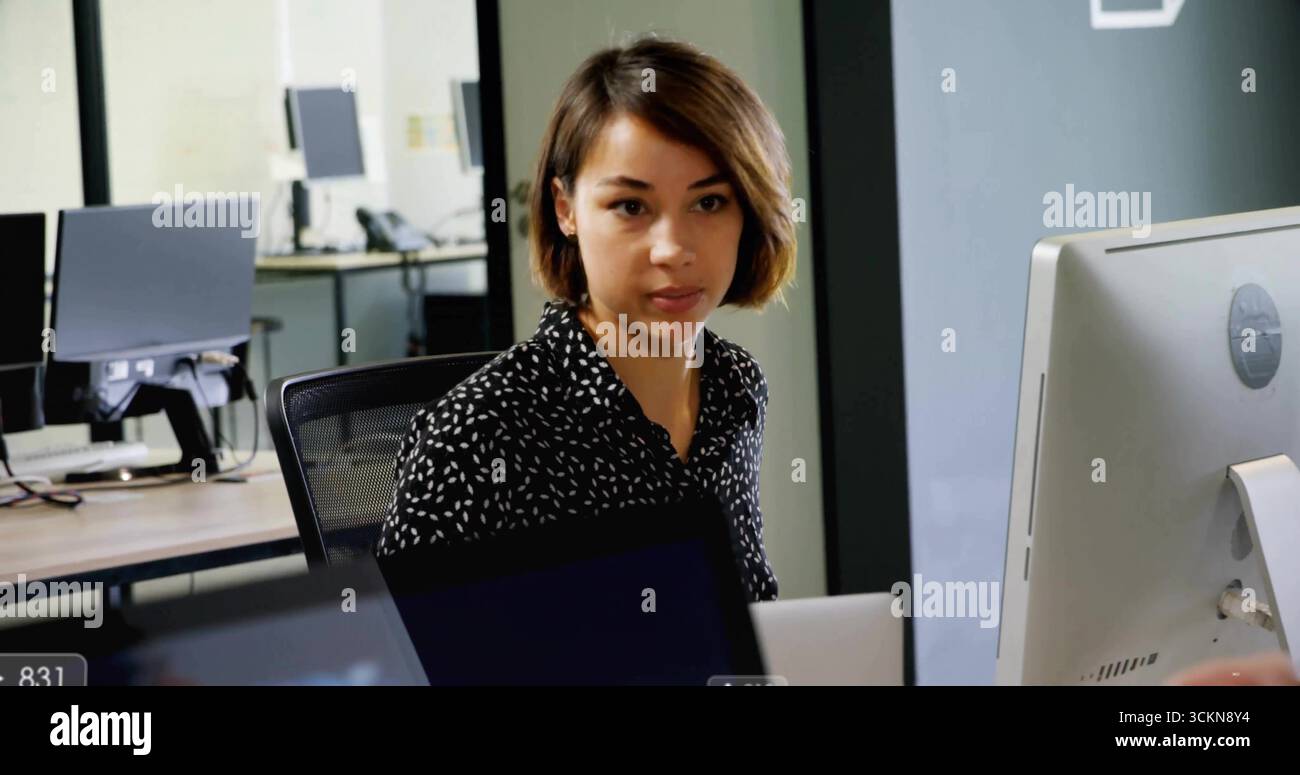 Tapant employé de bureau féminin se concentrant sur l'écran au bureau, avec ordinateur portable, cloison en verre Banque D'Images