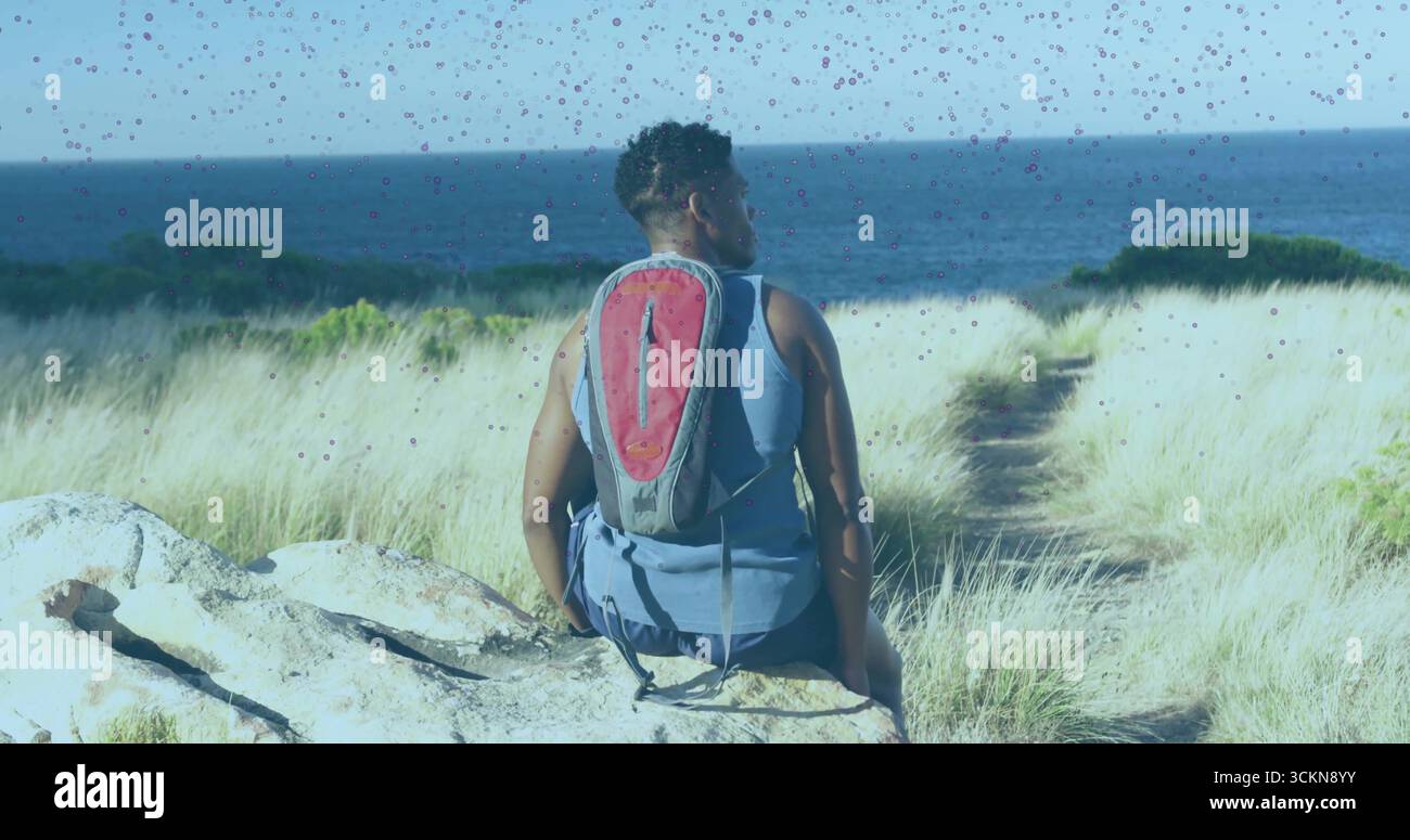 Homme assis portant le dessus bleu et sac à dos d'hydratation sur la dune de plage, sentier de sable à travers les herbes dune Banque D'Images