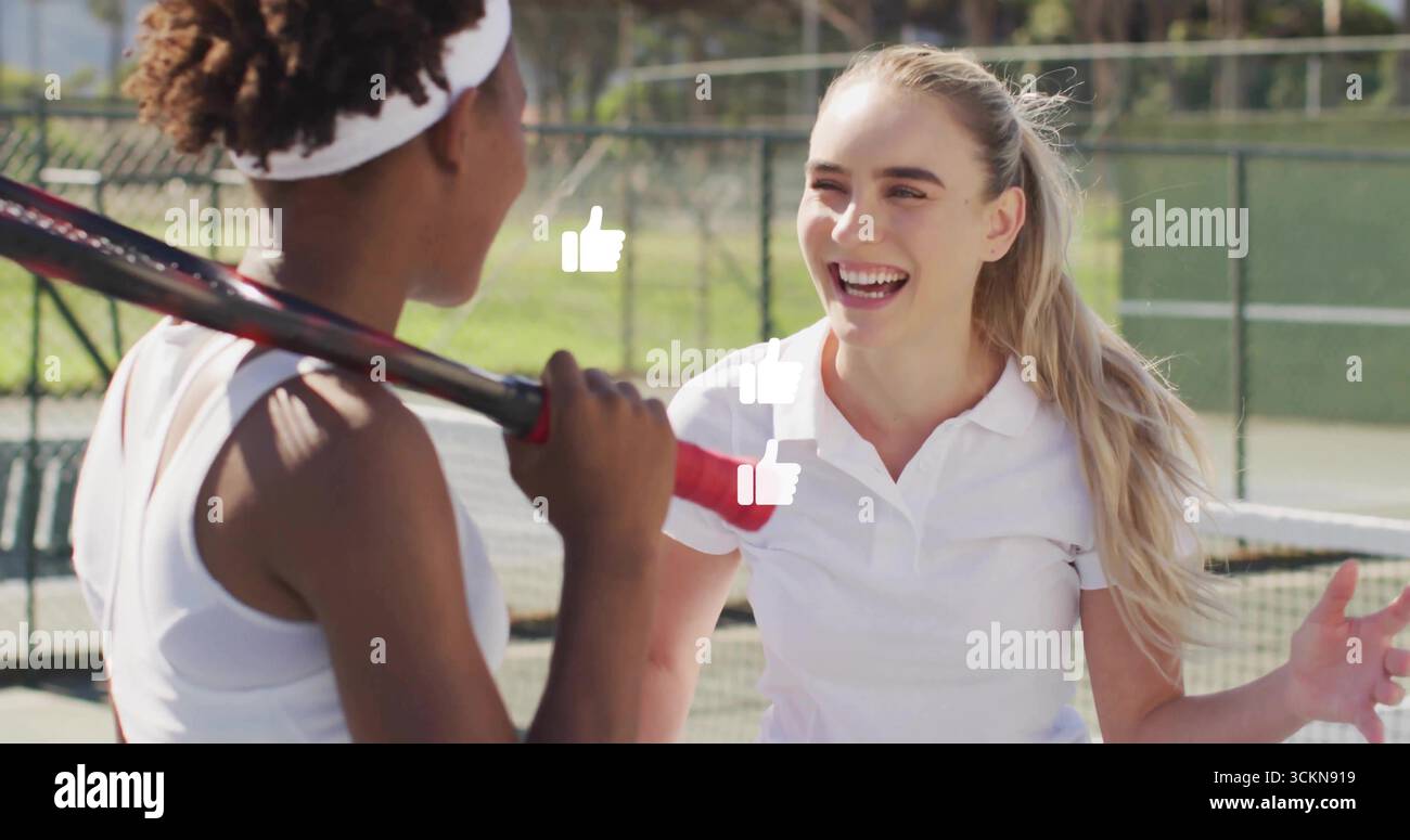 Joueurs de tennis souriants et parlants debout près du filet sur un court vert, avec bandeau de raquette et clôture Banque D'Images