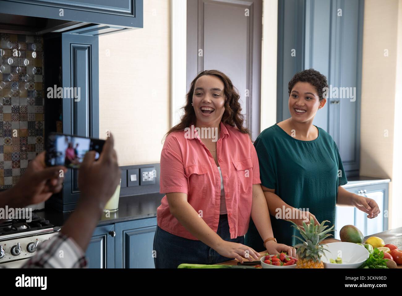 Diverses amies féminines tranchant l'ananas, arrangeant les fraises sur le comptoir avec smartphone Banque D'Images