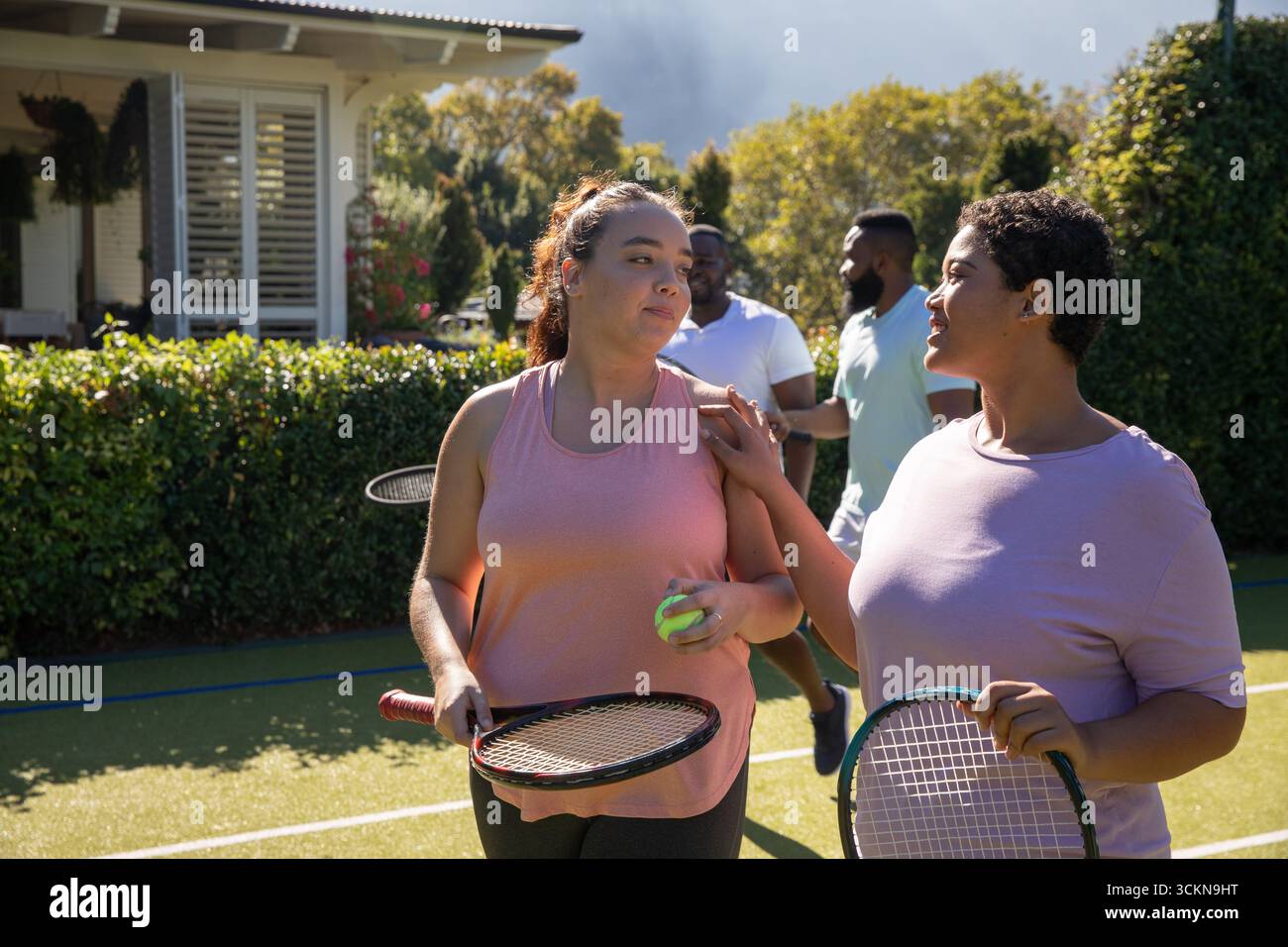 Divers amis marchant, bavardant sur le court de tennis en herbe avec des raquettes, balle et lignes, espace de copie Banque D'Images